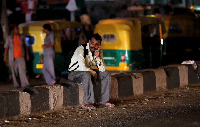 A man sits on a road divider as he waits for a bus in New Delhi, India.